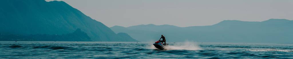 Banner ancho de Jetski on Delivery con una foto de fondo con un paisaje marítimo con una moto de agua a la derecha